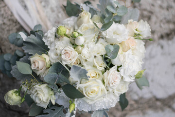 Beautiful bridal bouquet of white flowers and greenery, decorated with long silk ribbon lies on a gray textural background.
