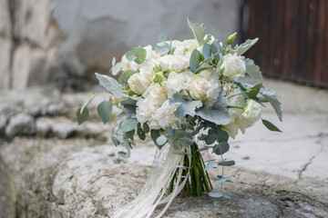 Beautiful bridal bouquet of white flowers and greenery, decorated with long silk ribbon lies on a gray textural background.