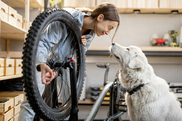 Young handywoman with her cute dog during a bicycle repairment in the home workshop or garage. DIY concept - Powered by Adobe