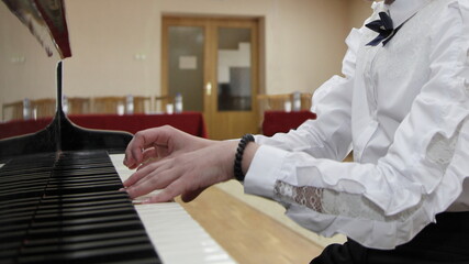 Fototapeta premium White hands of a young Caucasian piano girl playing the classical Grand piano against the background of an empty hall closeup, distance learning for music playing