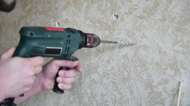 Man drills hole in marbled painted plaster wall surface. Male hands hold electric drill to make hole with drill beat rotating. Slow motion footage. DIY home improvement