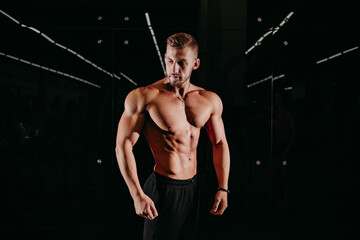 Fototapeta na wymiar Athletic shirtless young male fitness model holds the dumbbell with light isolated on dark background.
