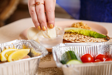 A woman's hand at the Easter Seder table dips maror and karpas in salt water.