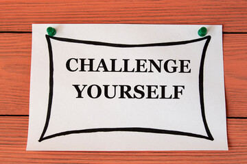 CHALLENGE YOURSELF - words on a white sheet on a brown wooden background