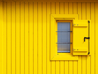 Ventana abierta en una fachada amarilla de una cabaña de madera