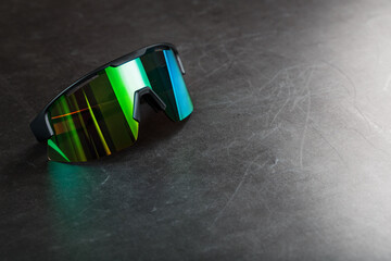 Sports glasses with a green mirrored lens on a black textured background.