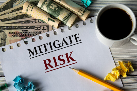 MITIGATE RISK - words on a white sheet against a background of banknotes, cups of coffee and pencil