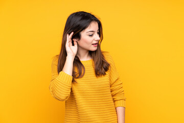 Young caucasian woman isolated on yellow background listening to something by putting hand on the ear