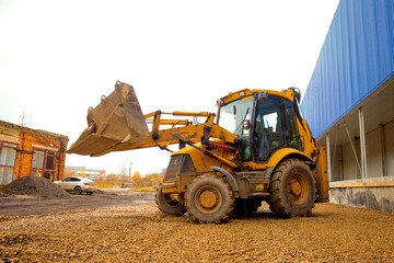 Obraz na płótnie Canvas a powerful yellow wheeled excavator against the background of rubble hills and a blue building, unloads rubble. Heavy equipment, construction site. selective focus