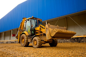 a powerful yellow wheeled excavator against the background of rubble hills and a blue building,...