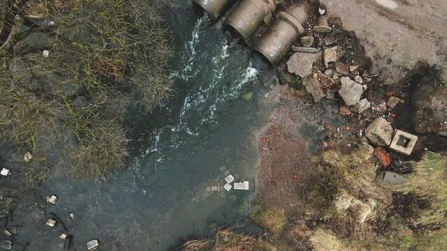 Flying over concrete sewers. Streams of water flow through concrete pipes. Polluted body of water in the park. The camera goes down.