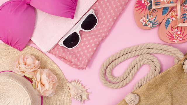Trendy accessories for beach and summer appear on pastel pink background. Stop motion flat lay