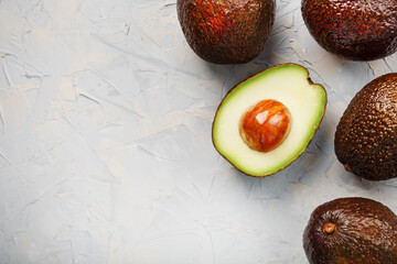 Avocado halves with whole Hass fruits on a background of gray concrete, stone or slate.