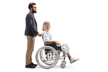 Full length profile shot of a bearded man pushing a young woman patient in a wheelchair