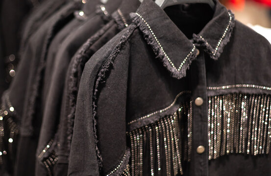 Trendy black denim shirts with braid and cowboy-style metal for women. Clothes hanging on hangers in the store
