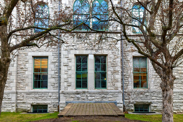 Exterior facade of an older limestone building framed between two apple trees showing paned windows, nobody