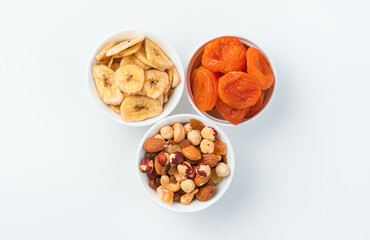 Dried apricots, dried banana and a mixture of nuts and candied fruits in three cups on a light background.