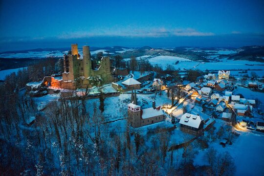 Luftaufnahme von Burg Hanstein und dem Dorf Rimbach im Winter am Abend mit Beleuchtung