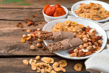 Granola bars, various nuts and dried fruits in a white plate on a wooden background.
