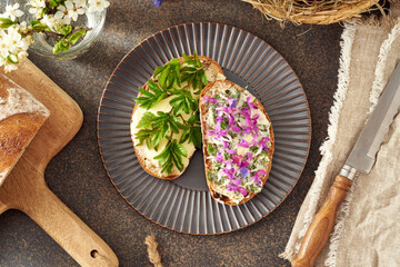 Two slices of sourdough bread with wild edible spring plants - goutweed leaves, purple dead-nettle and lungwort flowers