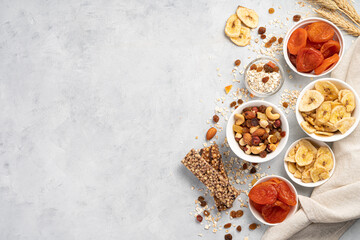 A set of nuts and dried fruits, a granola bar and raisins on a gray background.