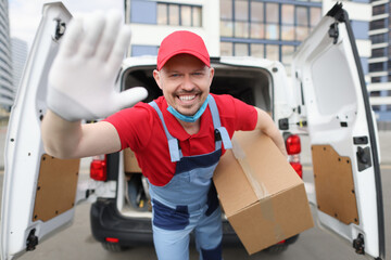 Smiling male courier holding large cardboard box on background of car