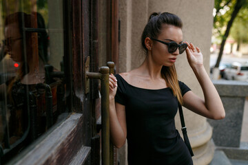 Profile of a beautiful sexy brunette girl in the big sunglasses walking around the city.