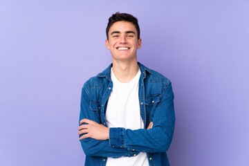 Teenager caucasian  handsome man isolated on purple background keeping the arms crossed in frontal position - obrazy, fototapety, plakaty
