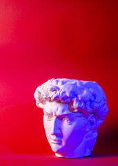 Gypsum statue of David's head. Michelangelo's David statue plaster copy isolated on red background. Ancient greek sculpture, statue of hero.