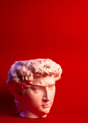 Gypsum statue of David's head. Michelangelo's David statue plaster copy isolated on red background. Ancient greek sculpture, statue of hero.