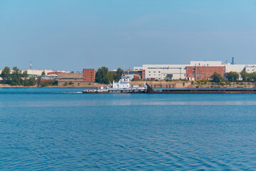 towboat pushes dry bulk cargo barge on the river past the industrial landscape