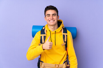 Teenager caucasian mountaineer man with a big backpack isolated on purple background giving a thumbs up gesture
