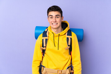 Teenager caucasian mountaineer man with a big backpack isolated on purple background having doubts and with confuse face expression