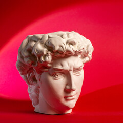 Gypsum statue of David's head. Michelangelo's David statue plaster copy isolated on red background. Ancient greek sculpture, statue of hero.