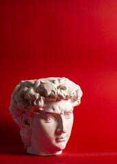 Gypsum statue of David's head. Michelangelo's David statue plaster copy isolated on red background. Ancient greek sculpture, statue of hero.