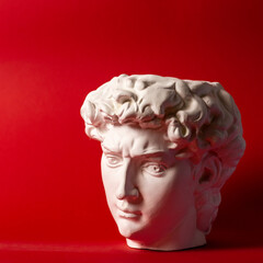 Gypsum statue of David's head. Michelangelo's David statue plaster copy isolated on red background. Ancient greek sculpture, statue of hero.