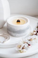 Fototapeta na wymiar Blooming apricot tree branches in vase and burning candle on round tray in home interior