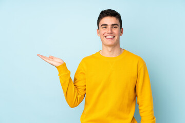 Teenager caucasian handsome man isolated on purple background holding copyspace imaginary on the palm to insert an ad