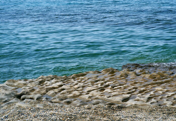 The surface of the coastal stone is uneven, wavy. The stone is worn down by the sea waves. Natural landscape with sea and rocky, altered sea, coast.