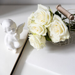 a white faience angel and three roses are on the table