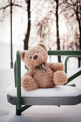 The toy bear was left in the winter at the children's playground