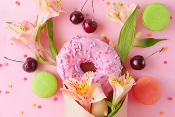 donat and fresh cherries, alstroemeria flowers, green and beige macaroons in a paper envelope on a...
