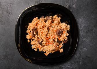 Uzbek pilaf with meat on a black plate on a dark background top view