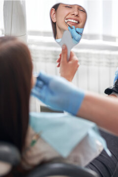 Happy young woman smiling checking out her perfect healthy teeth in the mirror, at the dentist office