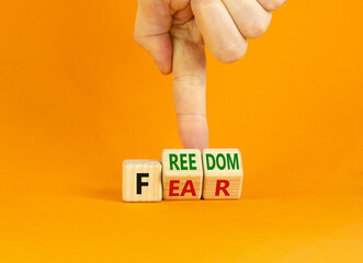 Freedom from fear symbol. Businessman turns wooden cubes and changes the word 'fear' to 'freedom'. Beautiful orange background, copy space. Business, motivational and freedom from fear concept.