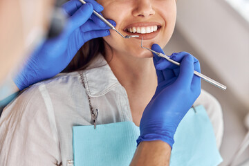 Cheerful positive dentist and client in dentistry. Female patient at dental procedure, doctor using dental instruments in modern dental clinic, close up.