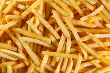 Large amount of golden-brown French fries sticks randomly arranged as a background close-up