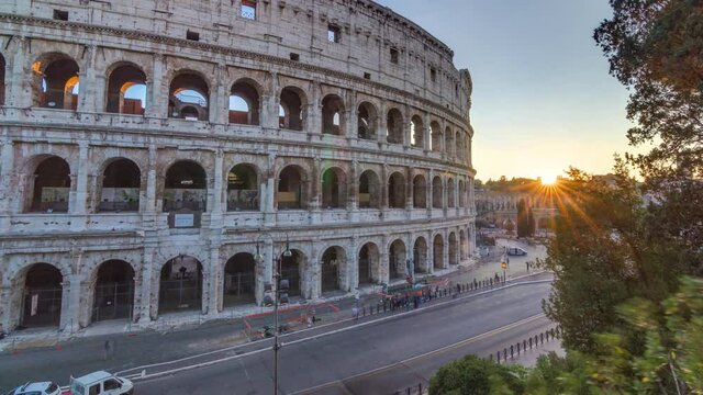Amphitheater Colosseum view at sunset timelapse top view. Rays of setting sun in trees. Traffic on the road with bus stop.