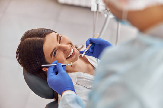 Portrait of young dentist in gloves examining teeth of female client in the hospital