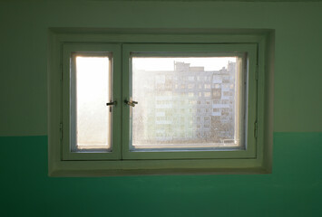 an uncleaned window in the stairwell at the entrance of a residential building, the sun is shining through the window.